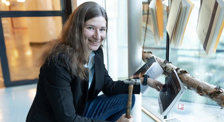 Anja Möslinger holding a hammer in front of her nailed thesis