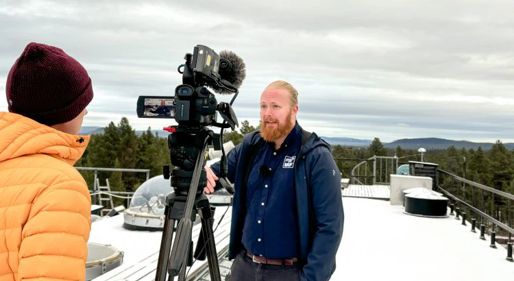 SVTs reporter intervjuar Daniel Kastinen på IRFs snötäckta tak, med mätutrustning under kupoler i bakgrunden