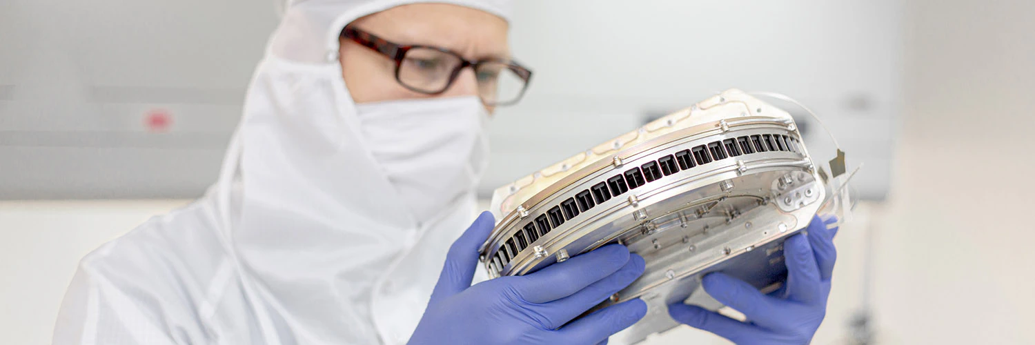 Engineer in protective clothing, with a prototyp of a satellite instrument in his hands